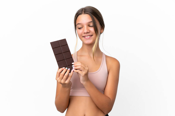 Little caucasian girl isolated on white background taking a chocolate tablet and happy - Photo, Image