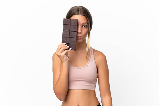 Little caucasian girl isolated on white background taking a chocolate tablet and surprised - Fotoğraf, Görsel