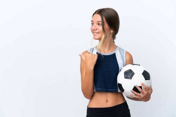 Маленькая кавказская девочка играет в футбол на белом фоне, указывая на сторону, чтобы представить продукт - Фото, изображение