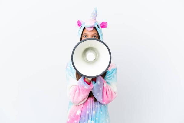 Piccola ragazza caucasica che indossa un pigiama unicorno isolato su sfondo bianco urlando attraverso un megafono - Foto, immagini