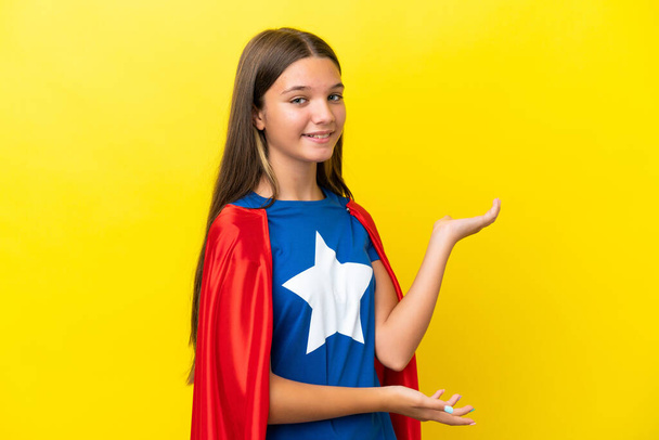 Little caucasian superhero girl isolated on yellow background extending hands to the side for inviting to come - Foto, immagini