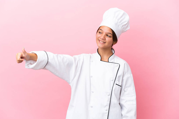 Pequeña chica chef caucásica aislado sobre fondo rosa dando un gesto pulgares hacia arriba - Foto, Imagen