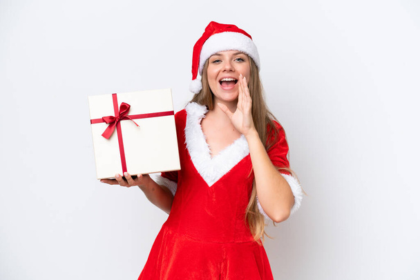 Young caucasian woman dressed as mama noel holding gift isolated on white background shouting with mouth wide open - Photo, Image