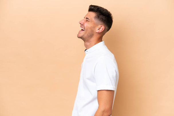 Giovane uomo caucasico isolato su sfondo beige ridendo in posizione laterale - Foto, immagini