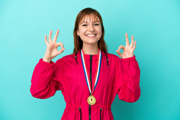 Zrzka dívka s medailemi izolované o modré pozadí ukazující ok znamení s prsty - Fotografie, Obrázek