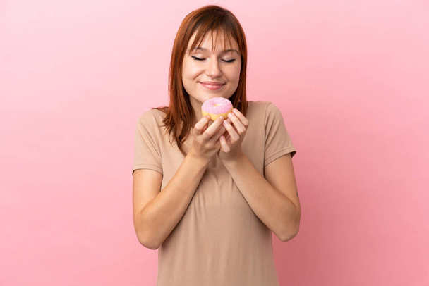 Redhead girl isolated on pink background holding a donut - 写真・画像