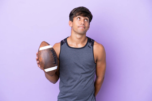 Young man playing rugby isolated on purple background and looking up - Photo, Image