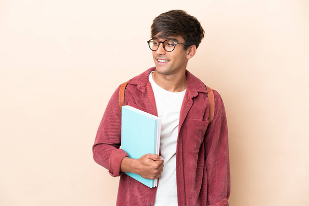 Jovem estudante caucasiano homem isolado em fundo ocre olhando para o lado e sorrindo - Foto, Imagem