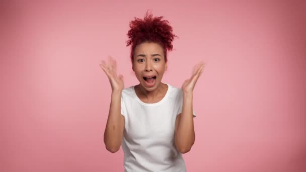 Portrait shocked scared curly redhead African American woman waving hands looking camera. Panic African female in white t-shirt standing on isolated pink background. People emotions lifestyle concept - Footage, Video