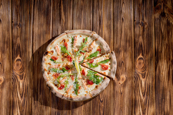 Pizza with salmon, mozzarella, cherry tomatoes, arugula, lemon and parmesan. Italian cuisine on a woden background. - Фото, зображення