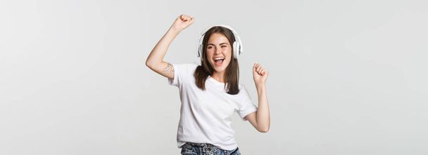 Ελκυστική χαρούμενη κοπέλα που χορεύει με ασύρματα ακουστικά, ακούει μουσική. - Φωτογραφία, εικόνα