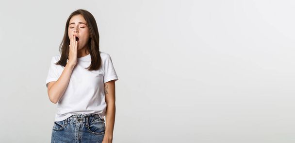 Portrait of attractive young female student yawning tired, feeling sleepy, white background. - Foto, afbeelding