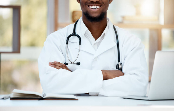 Healthcare, stethoscope and doctor with crossed arms at desk for support, consultation and wellness. Medicine, medical worker and black man sitting in hospital or clinic with smile, laptop and book. - Foto, immagini