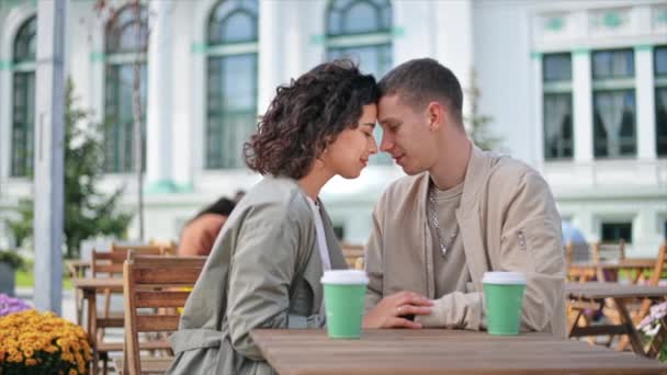 Um casal romântico ao ar livre perto de um café. De mãos dadas, a sorrir com os olhos fechados, café na mesa. Atmosfera de outono. Movimento lento - Filmagem, Vídeo
