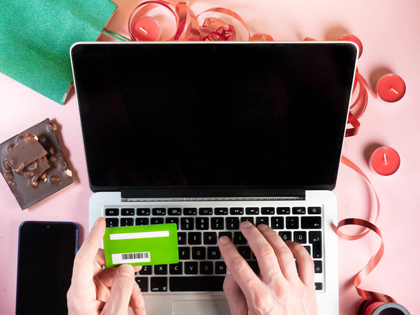 Top view of man making online shopping buying gifts with credit card. Gift, candles, chocolate, ribbons on pink background. Copy space - Foto, imagen