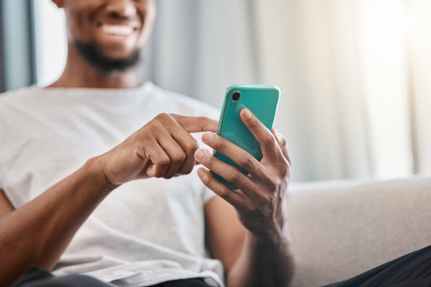 Hands, phone and social media with a black man typing a text message while sitting on a sofa in his home. Mobile, communication and networking with a male chatting from the living room in his house. - Фото, изображение