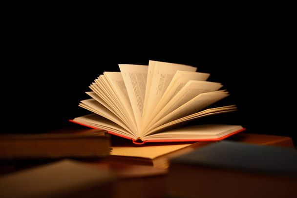 Open book lit by golden warm light against black background. Reading, wisdom concept - Foto, imagen