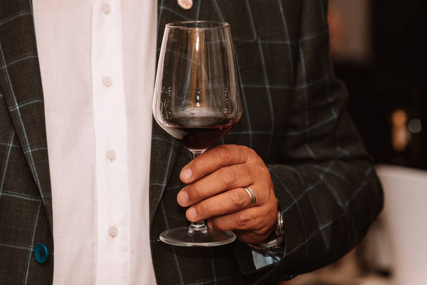 Glass of red wine held by a person at a premium wine tasting with friends and wine lovers. - Photo, image