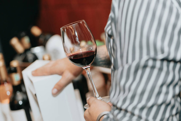 友人やワイン愛好家とのプレミアムワインの試飲で人が保持する赤ワインのガラス. - 写真・画像