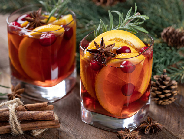 Mulled wine with orange slices, cranberries and spices on rustic wooden table with Christmas tree decoration in background - Photo, image