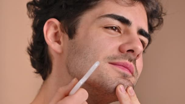 Un joven caucásico con barba de barba está haciendo un masaje facial usando un Gua Sha - Imágenes, Vídeo
