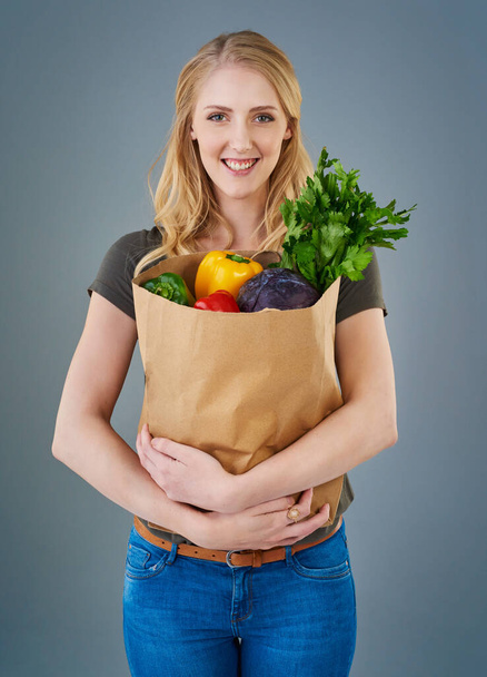 Her mom taught her to eat her veggies. Cropped studio shot of a young woman holding a paper bag full of vegetables - Foto, Imagem