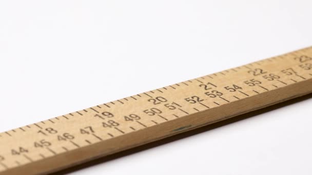 Detailní záběr na dřevěnou měřicí tyč s měřítky v palcích a centimetrech klouzání na bílém pozadí. - Záběry, video
