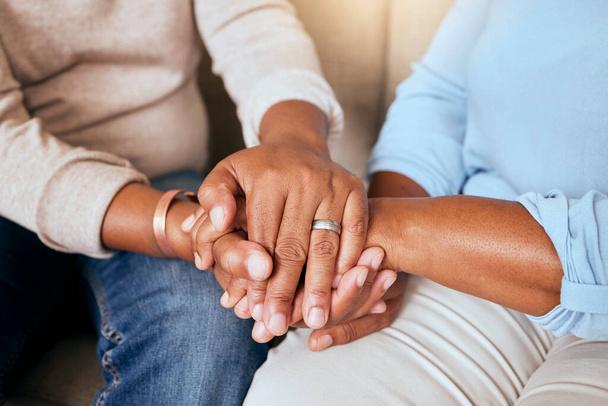 Support, love and closeup of people holding hands for comfort while sitting on a sofa together. Compassion, sympathy and friends praying, bonding and healing together in the living room of a house - Foto, afbeelding