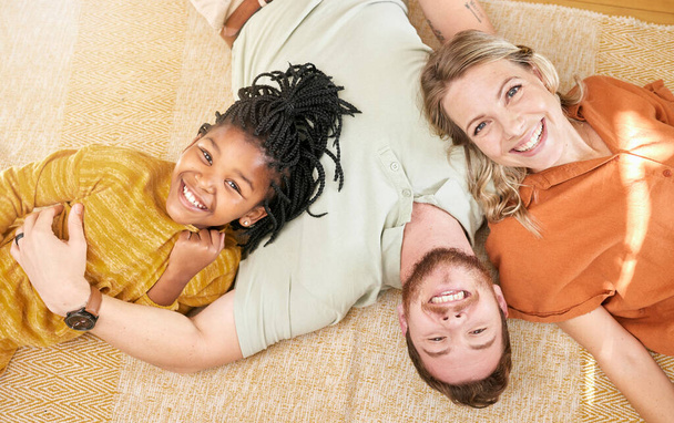 Ευτυχισμένοι, οικογένεια και το πορτρέτο υιοθεσίας πάνω άποψη της καυκάσιας μητέρας και του μπαμπά με μαύρο παιδί στο σπίτι. Χαλαρώστε, διαφυλετικό και χαμόγελο του παιδιού μαζί με ανάδοχη μαμά και τον πατέρα σε ένα χαρούμενο σπίτι - Φωτογραφία, εικόνα