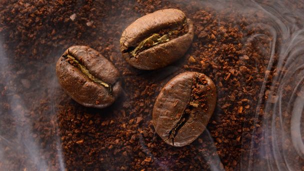 Three coffee beans lie on ground coffee, light aromatic coffee smoke, close-up and copy space. - Photo, Image