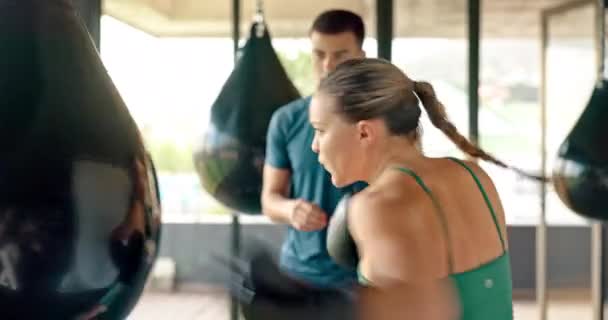Coach, vrouw en bokszak tijdens training, training en praten in de sportschool voor gezondheid, welzijn en fitness. Man trainer, vrouwelijke atleet en bokser praktijk, hebben gesprek, voor oefening en routine. - Video