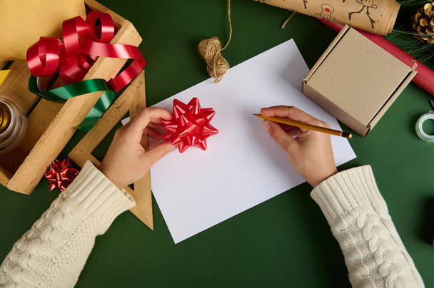 Close-up kobieta za pomocą drewnianej kredki, rysunek, pisanie na białym papierze arkuszu z miejsca reklamy kopii, na zielonej powierzchni, z opakowań kreatywnych i dekoracyjnych materiałów, ozdoby do pakowania prezentów świątecznych - Zdjęcie, obraz