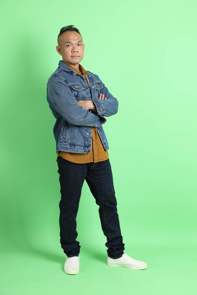 40s dospělý asijský muž s džínovou košilí stojící na zeleném pozadí. - Fotografie, Obrázek
