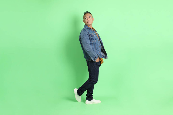 Los años 40 adulto asiático hombre con camisa de jean de pie sobre el fondo verde. - Foto, imagen