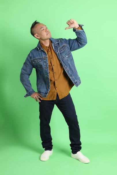 The 40s adult Asian man with jean shirt standing on the green background. - Photo, Image
