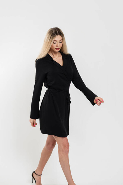 Fashion blonde woman in black stylish elegance dress with legs walks on the white background in studio - Foto, Imagen