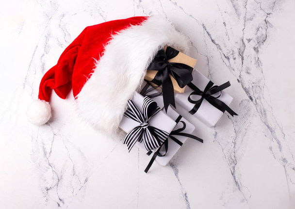 Presents in wrapped boxes in red Santas hat on white marble background. Minimalists Christmas. Top view. Place for text. - Фото, зображення