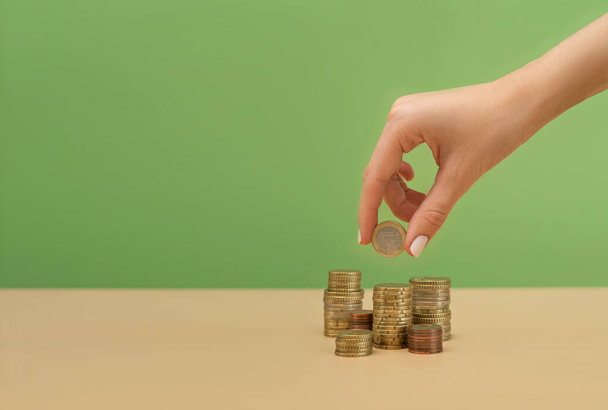 Female hand holding a coin above the stack of coins. Finance concept - Foto, Imagen