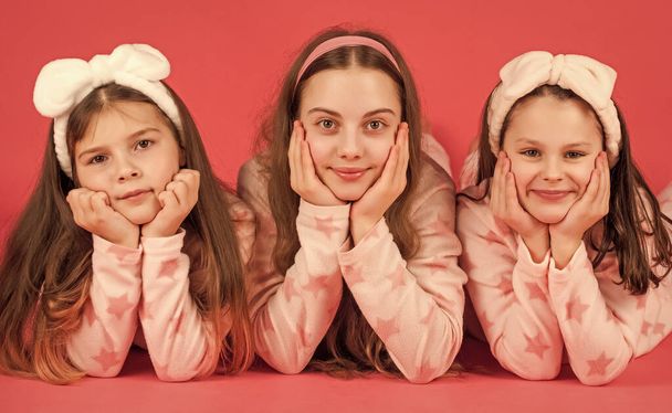 Portrait of happy girls lying with cheeks propped on hands in pajamas pink background. - Foto, Imagen