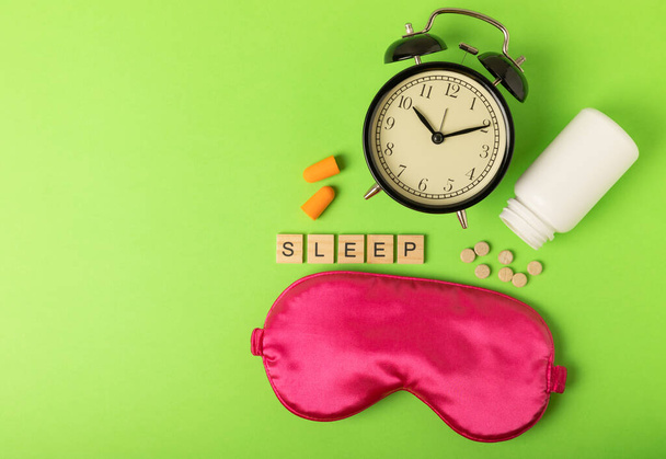 Nukkuva naamio, herätyskello, pillerit, korvatulpat ja kaiverrus SLEEP vihreällä taustalla. Lepoa, unen laatua, hyvää yötä, unettomuutta ja rentoutumista. Näkymä ylhäältä. tasainen - Valokuva, kuva
