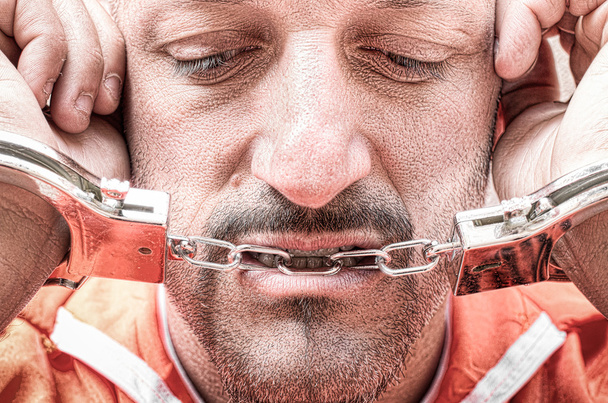 Sad depressed detained man with handcuffs in prison - Handcuffed inmate prisoner in jail with orange clothes - Crispy desaturated dramatic filtered look - Dead man walking concept and death penalty - Photo, Image
