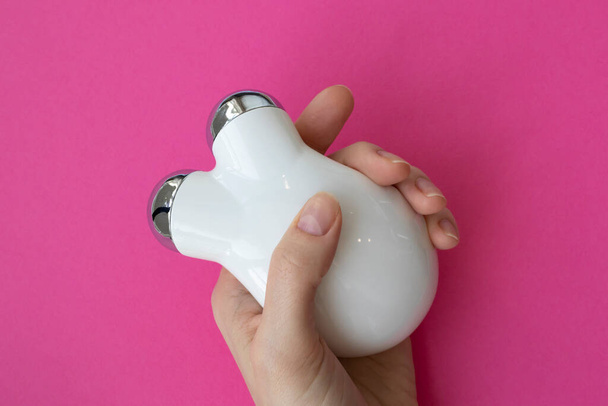 Συσκευή μασάζ προσώπου για ρυτίδες. Συσκευή μικρορευμάτων στο χέρι μιας γυναίκας σε ροζ φόντο - Φωτογραφία, εικόνα