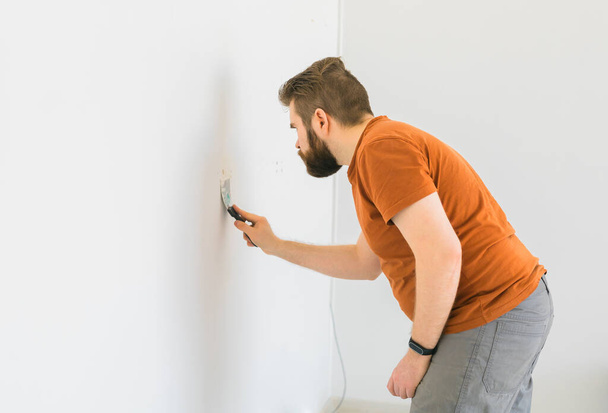 Человек сглаживает поверхность стены с помощью стенной мельницы. Мужчина измельчить белую штукатурку стены - ремонт и ремонт - Фото, изображение