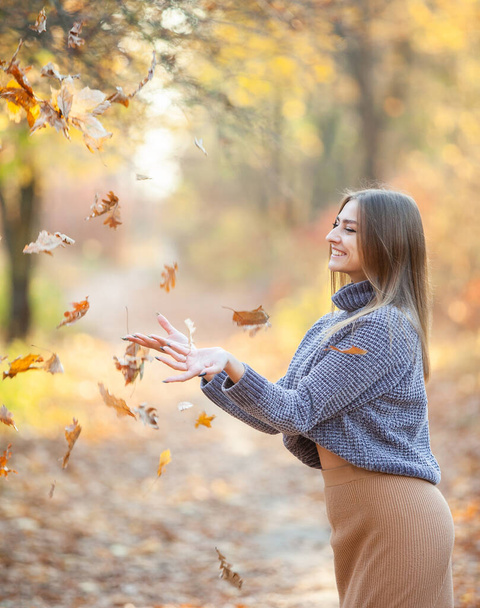 Zabawa, wesoła młoda kobieta rzucająca opadłe liście w jesiennym lesie. - Zdjęcie, obraz