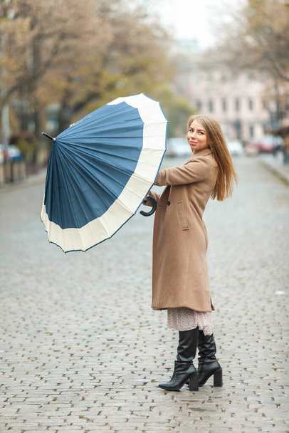 Vrij mooie vrouw in een jas wachtend op de regen opent paraplu in de stad - Foto, afbeelding