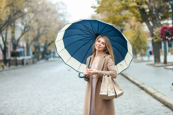 Femme heureuse en manteau avec parapluie tenant des sacs à provisions en ville, vente de shopping d'automne - Photo, image
