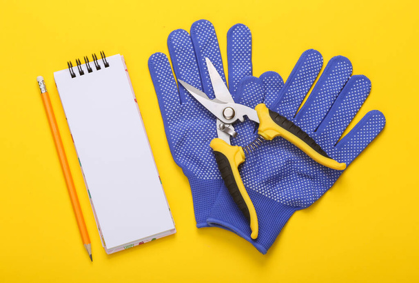 Pruner ogrodowy z rękawiczkami roboczymi i notatnikiem na żółtym tle. Leżeć płasko. Widok z góry - Zdjęcie, obraz
