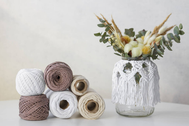 A composition with balls for knitting and a jar with dried flowers decorated in the macrame technique. Side view, flat lay, copy space. High quality photo - Foto, Bild
