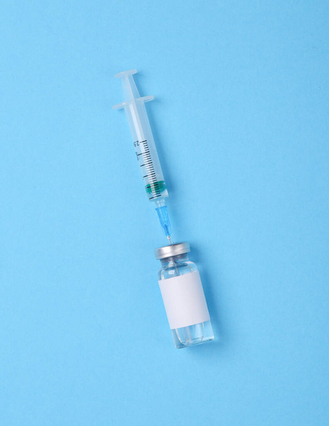 Flacone di vaccino con etichetta bianca per il marchio e siringa su fondo blu. Vaccinazione Covid 19 - Foto, immagini