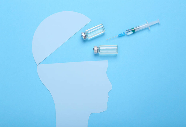 Cabeza humana de silueta abierta con frasco de vacuna y jeringa sobre fondo azul - Foto, imagen